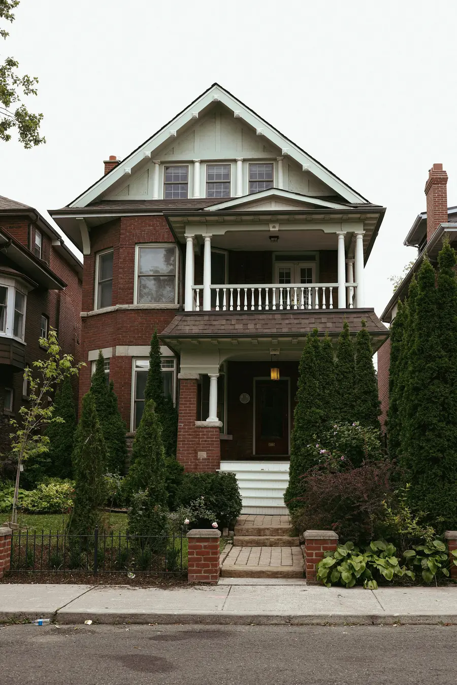 Two-storey red brick house with a white-columned front porch and evergreen shrubs