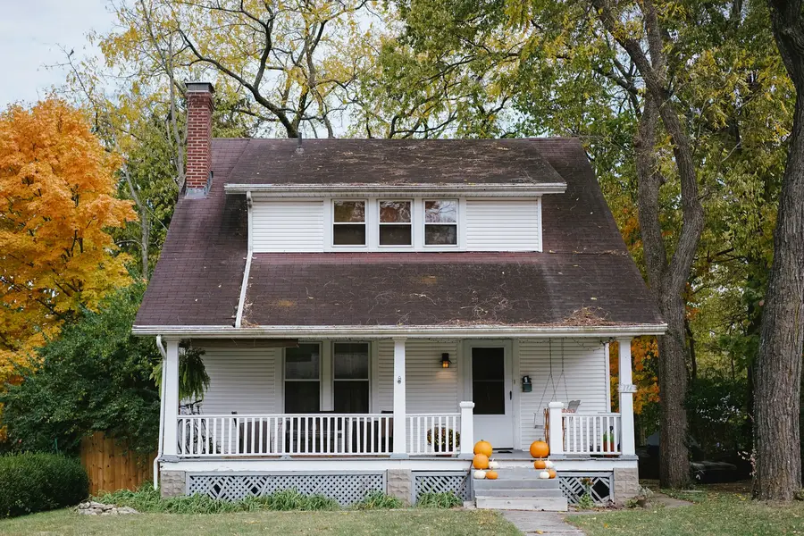White one-and-a-half-storey house with a front porch under autumn trees
