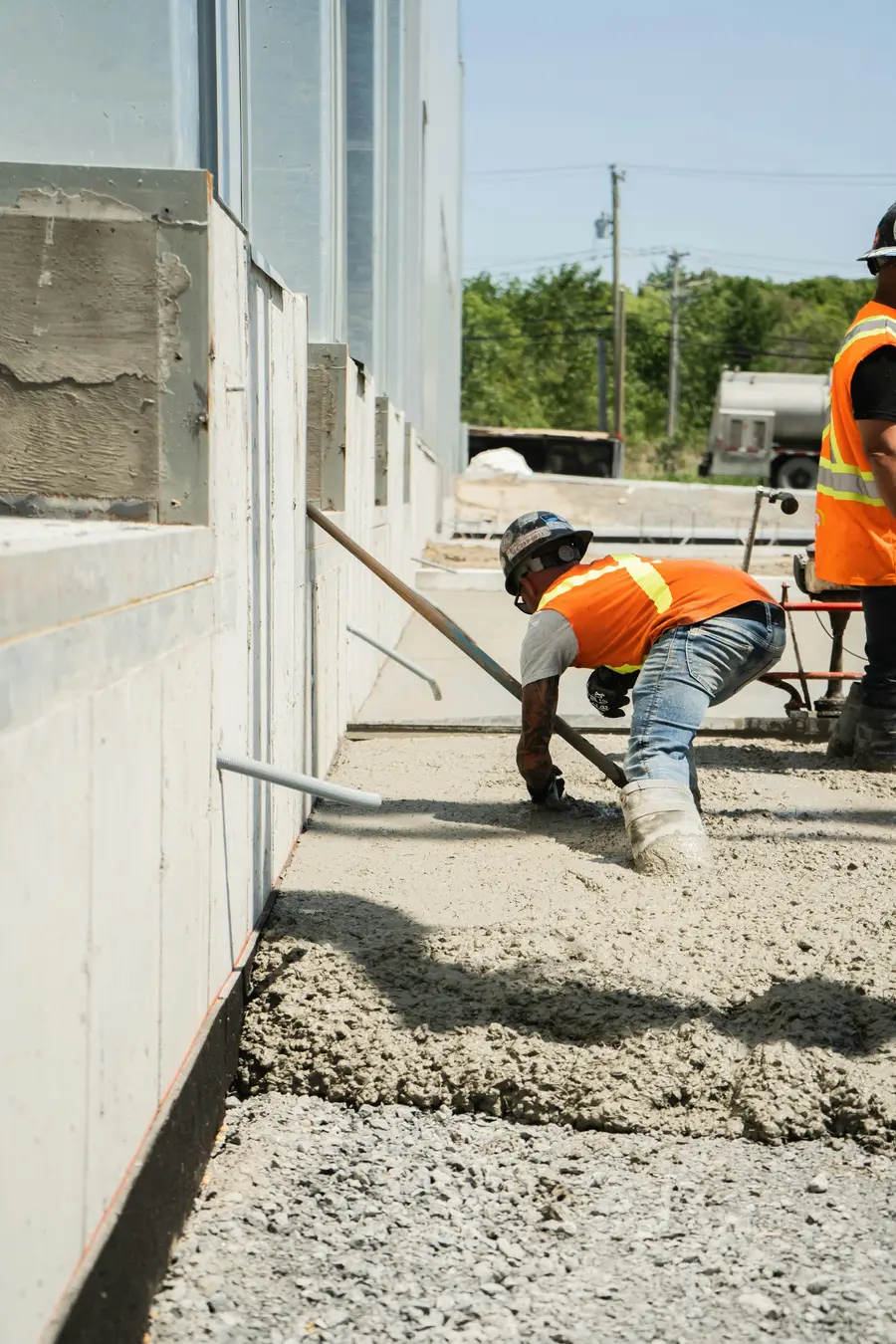 Worker in a high-visibility vest raking gravel level along a foundation wall