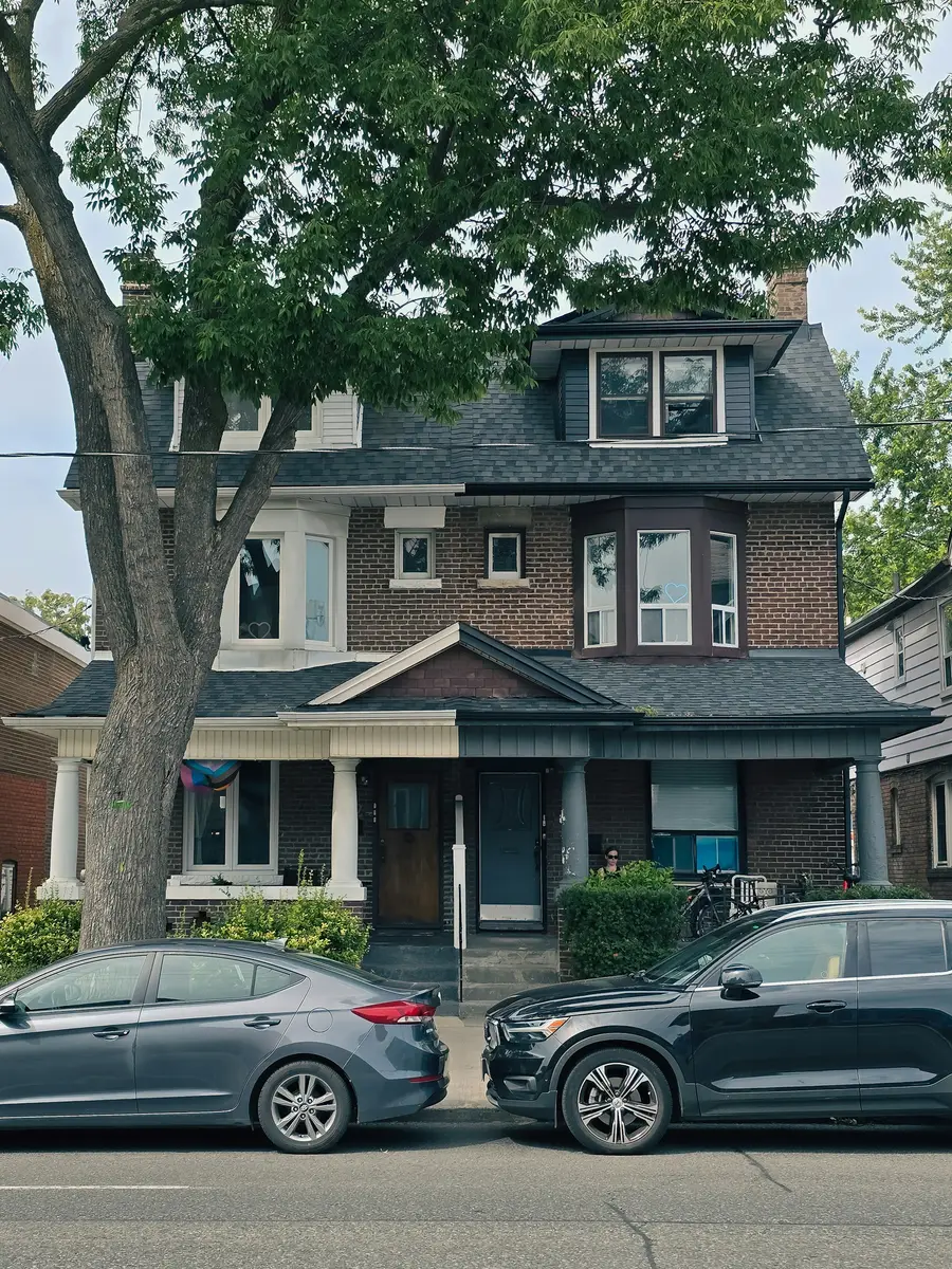 Dark brick two-storey house with a covered porch behind a large street tree