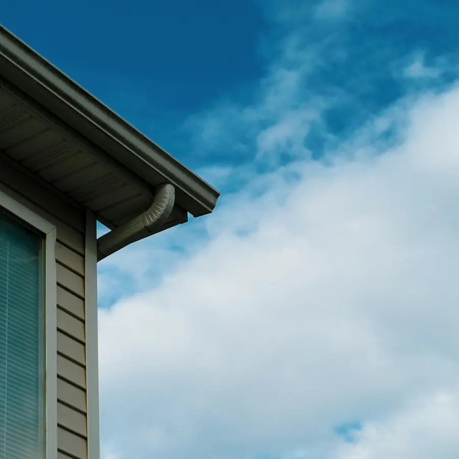 Eavestrough and downspout at the corner of a house with grey siding