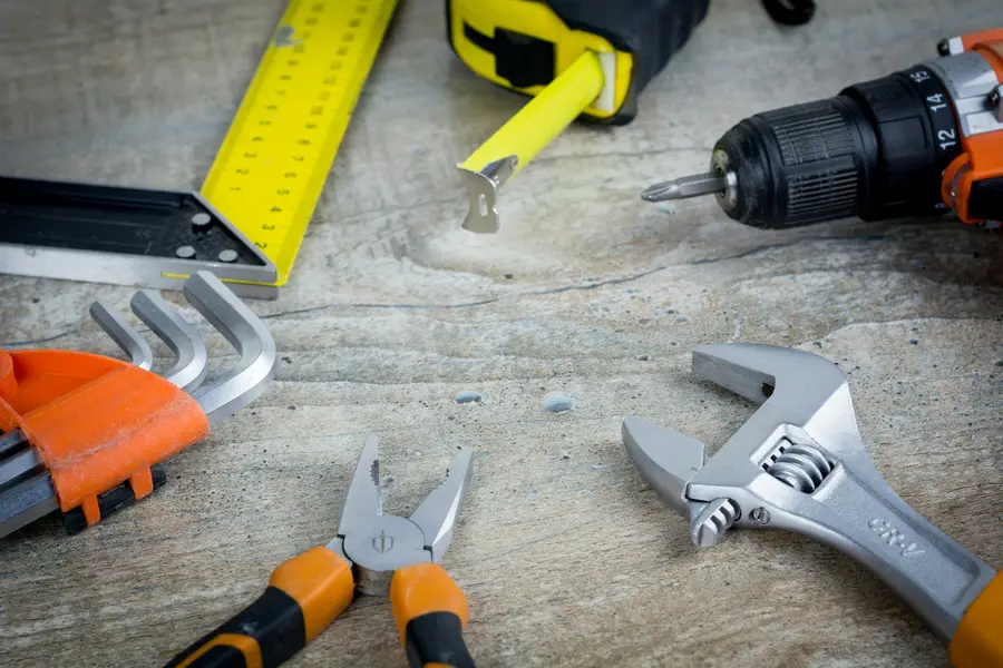 Tape measure, drill, pliers and an adjustable wrench laid out on a concrete floor