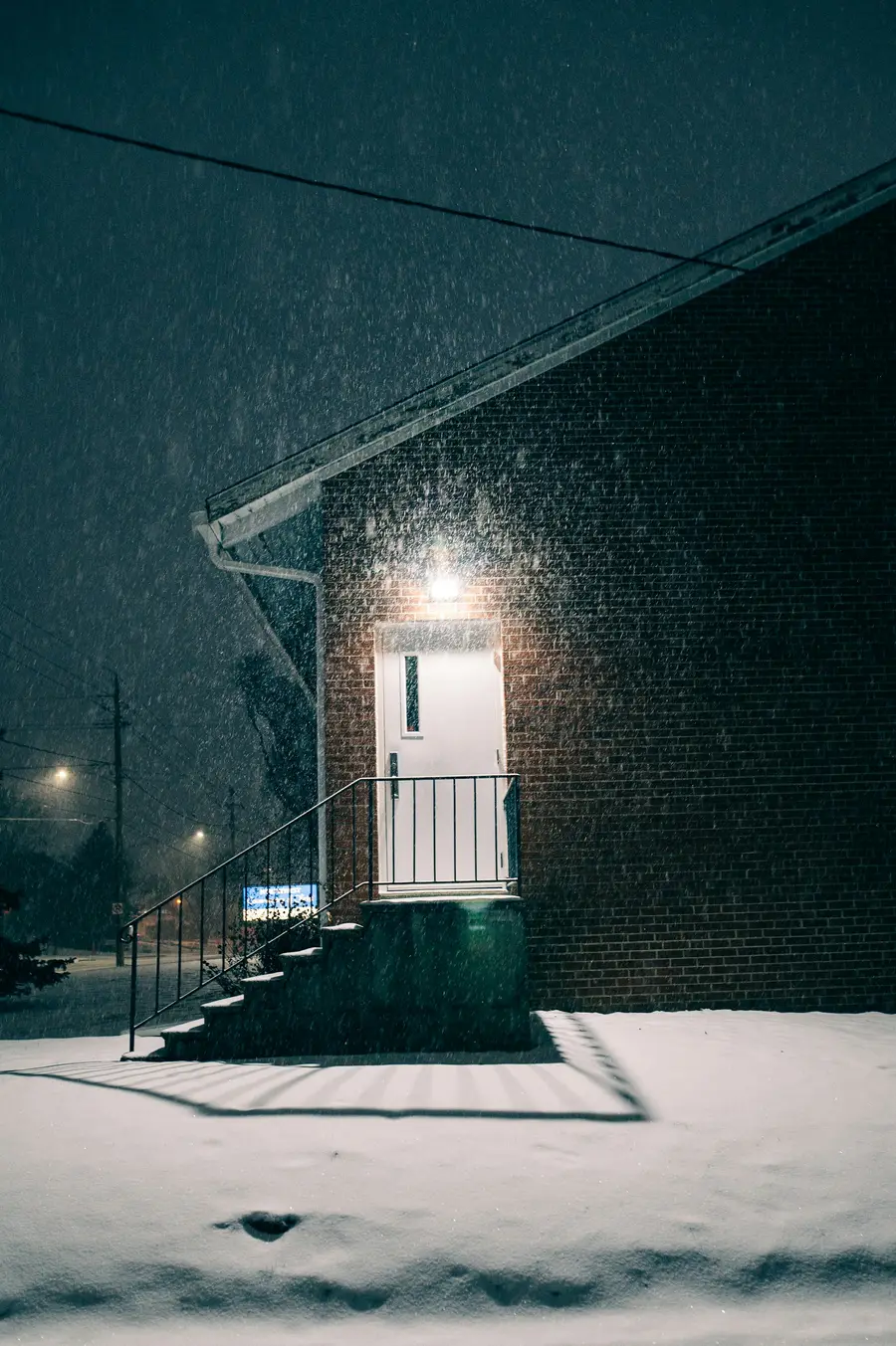 Brick house entrance lit by a porch light during a night snowfall