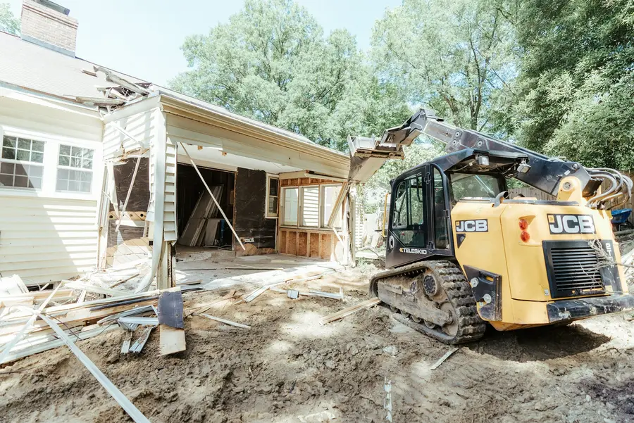 Compact track loader working on bare ground beside a white house