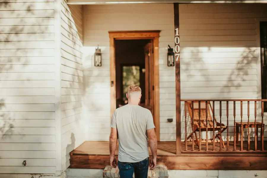 Man walking up to the wooden front door of a house with a covered porch