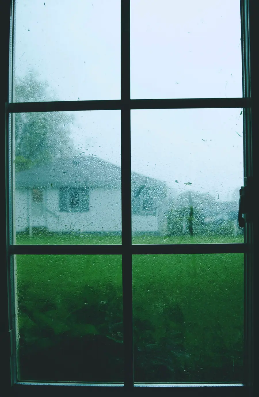 View through a rain-covered window toward a bungalow across the street