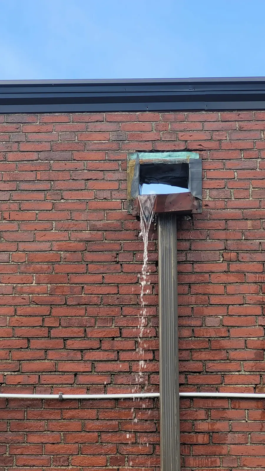 Water pouring from a metal roof scupper down a red brick wall
