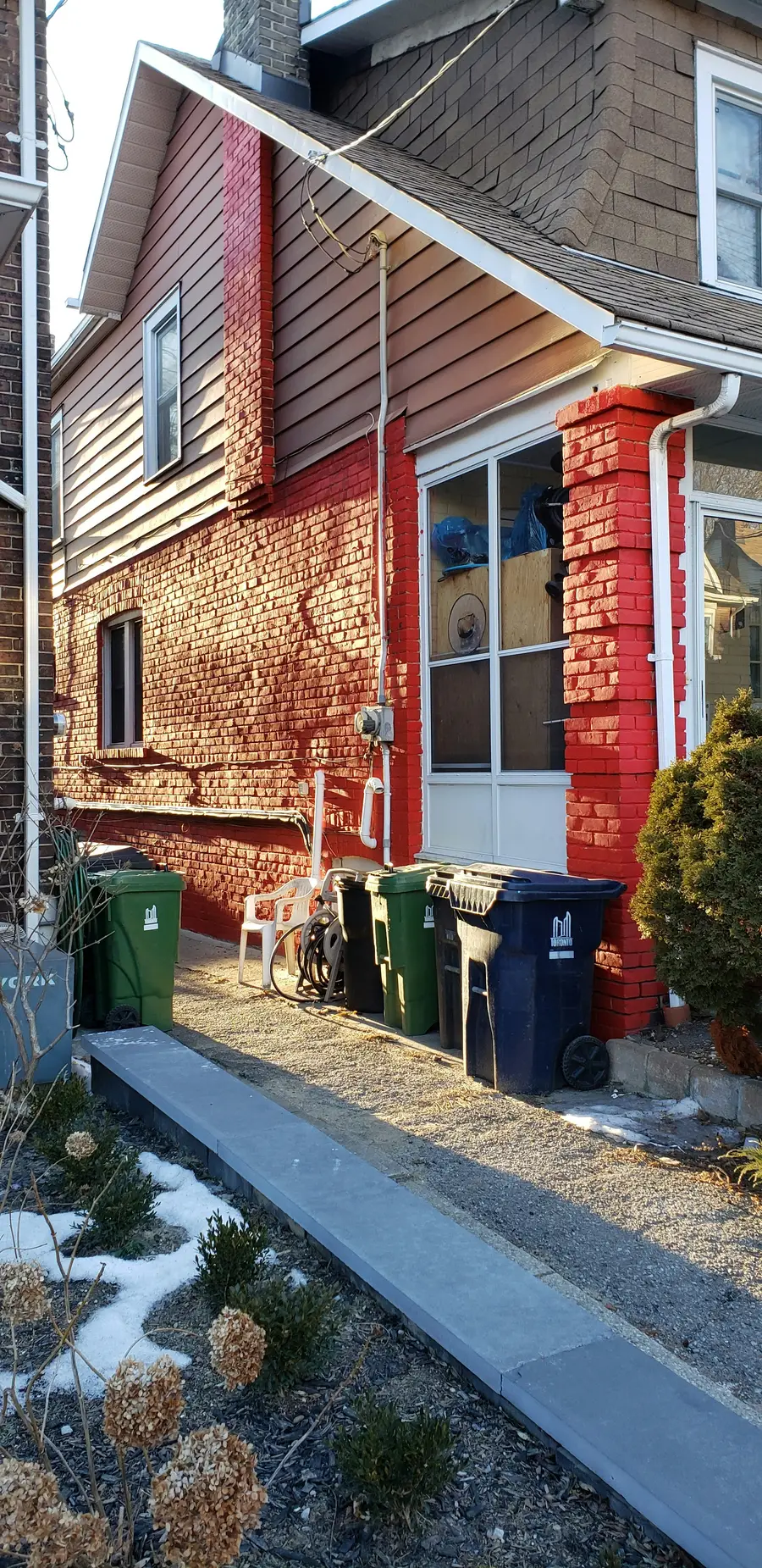 Narrow side yard of a red brick house with downspouts and waste bins
