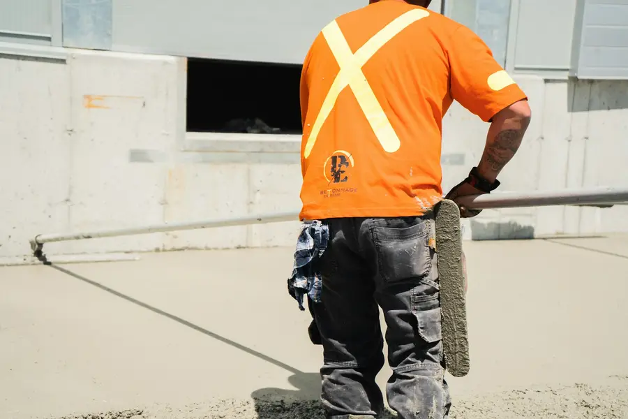 Worker in an orange high-visibility shirt finishing concrete beside a foundation wall