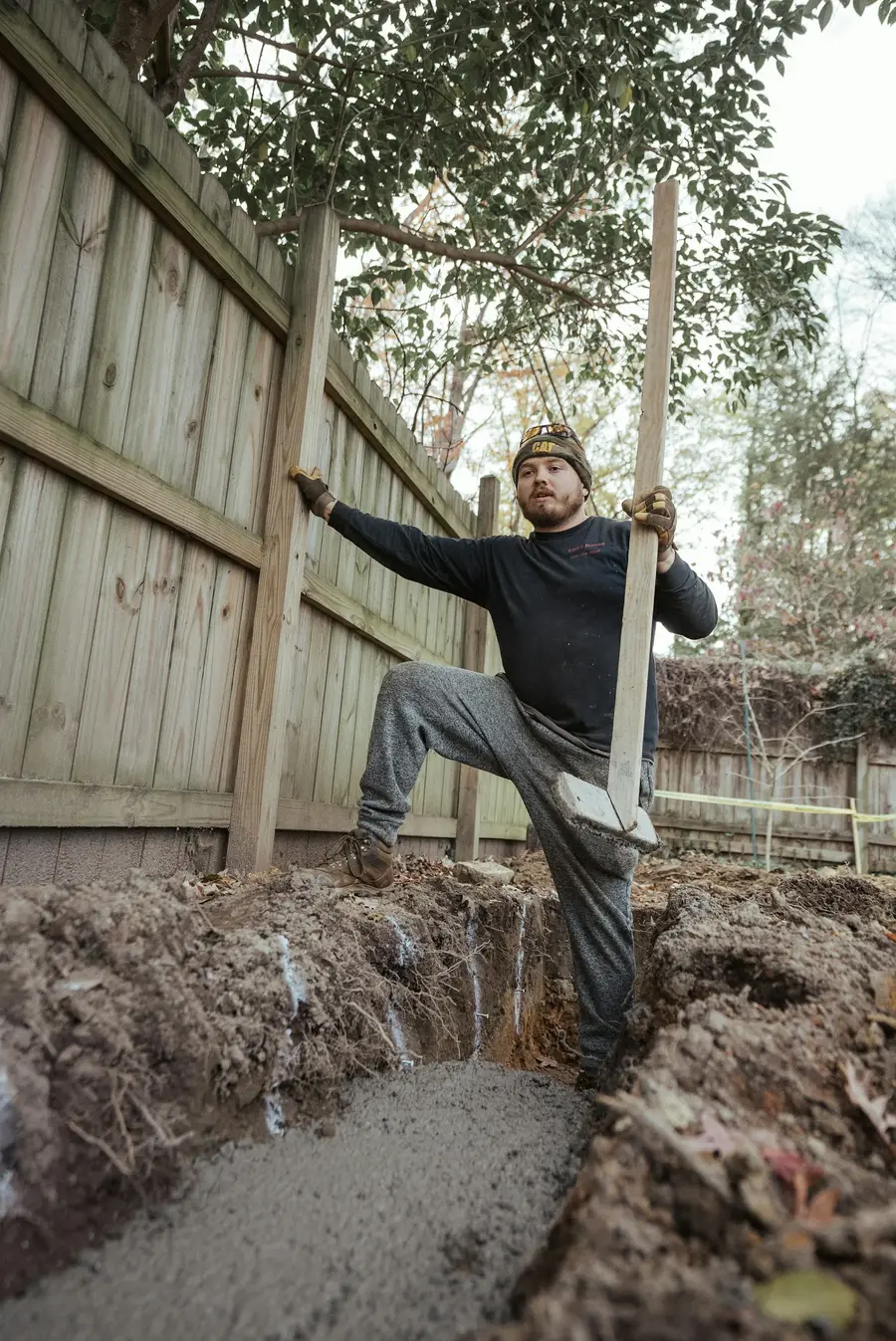 Worker standing in an excavated trench beside a wooden fence